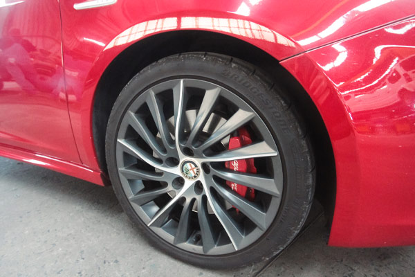 Close up photo of the front wheel of a car. The car is red and the wheel has red sports brakes fitted to it.